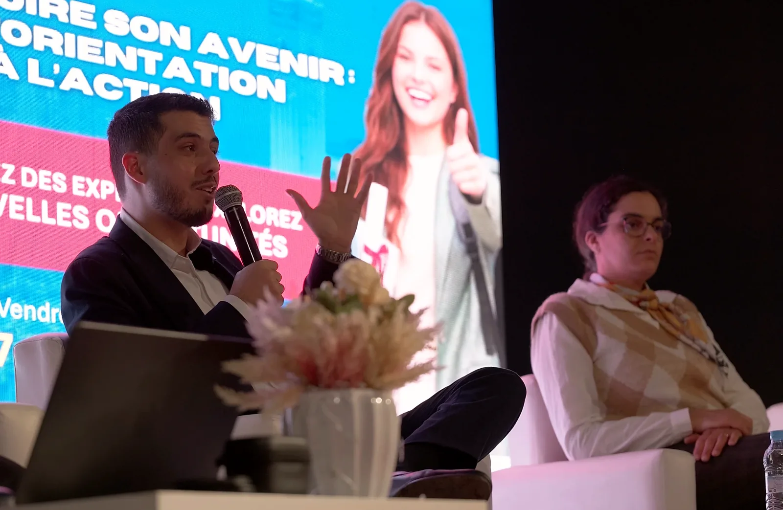 Un intervenant s'exprime au micro lors d'une table ronde sur l'orientation, à côté d'une participante