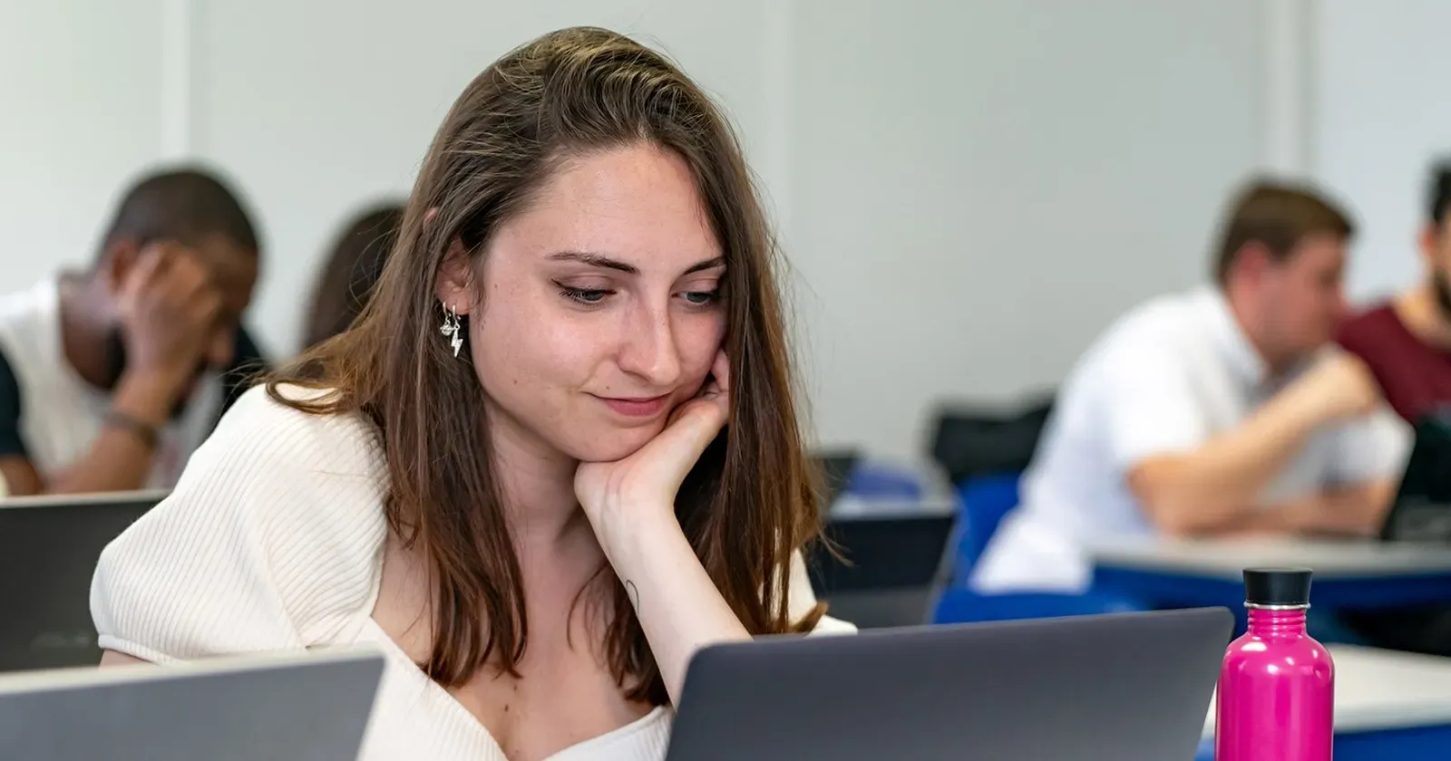 Une apprenante appuyée sur sa main suit un cours, entourée d'autres étudiants.