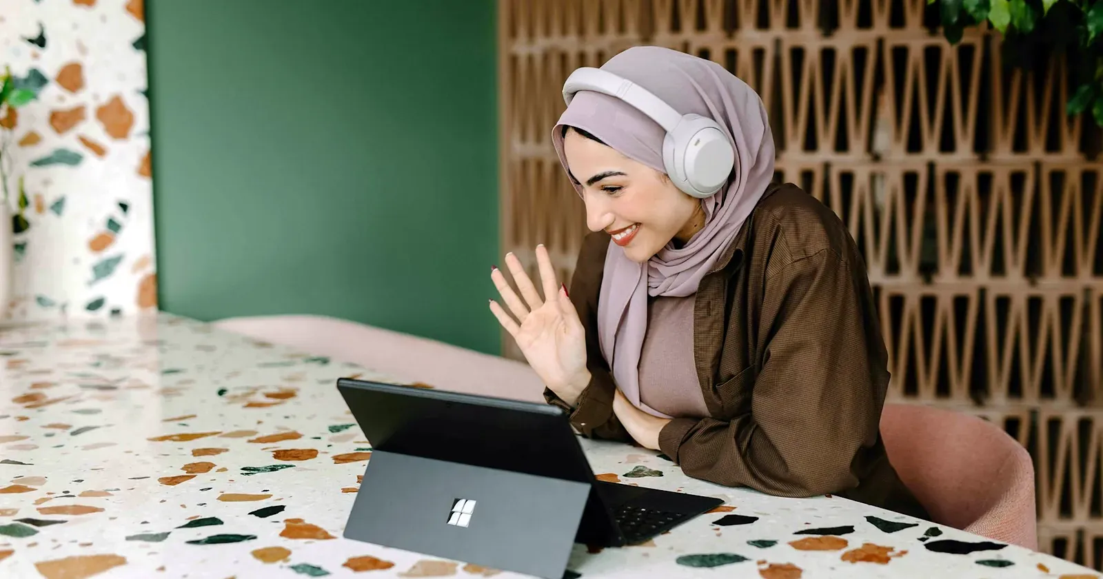 Une femme portant un casque salue son écran lors d'un cours à distance