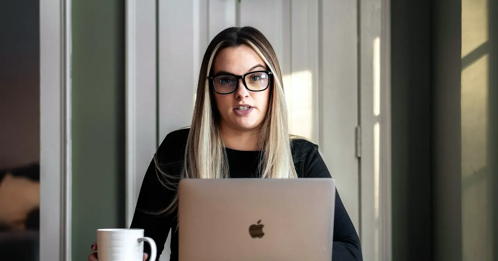 Une jeune femme à lunettes travaille sur son ordinateur portable, une tasse devant elle